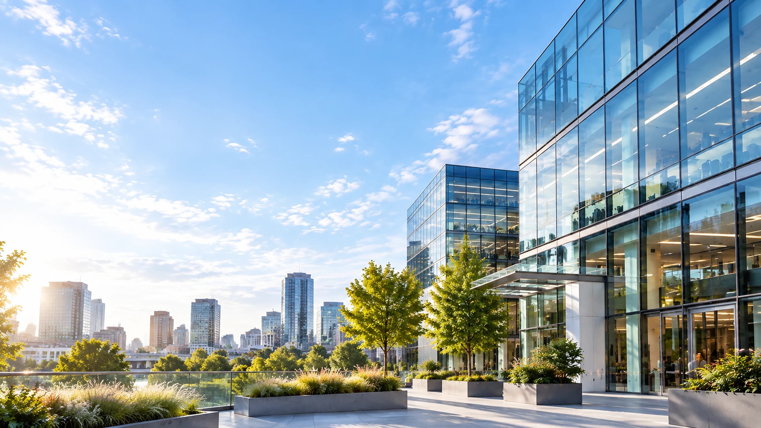 A modern glass office building with a landscaped terrace overlooking a city skyline